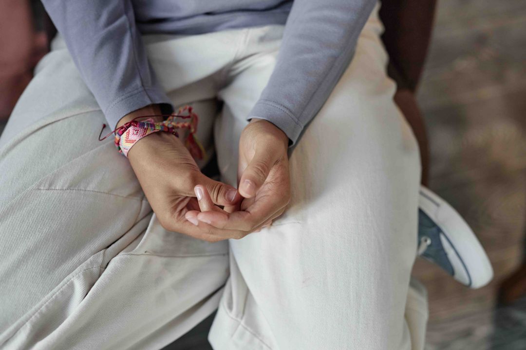 A young person's hands resting on their lap with a friendship bracelet