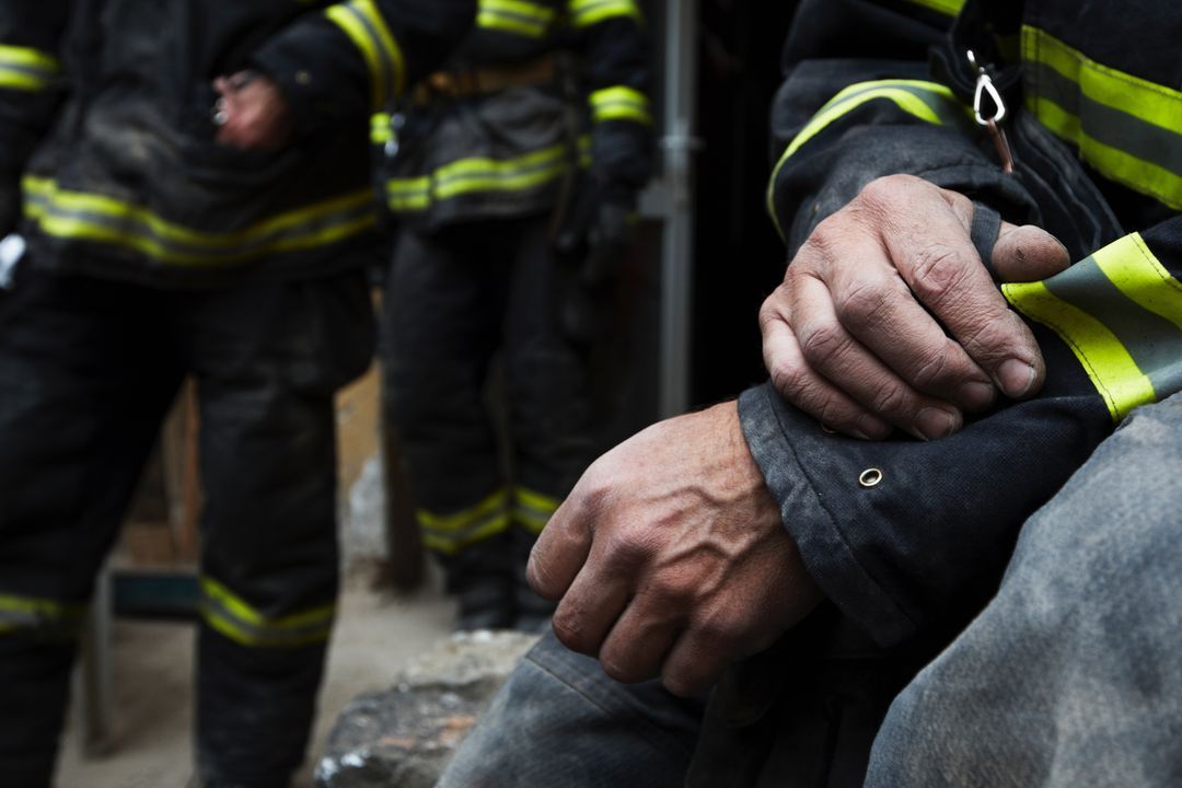 A firefighter's weathered hands clasped while resting in turnout gear